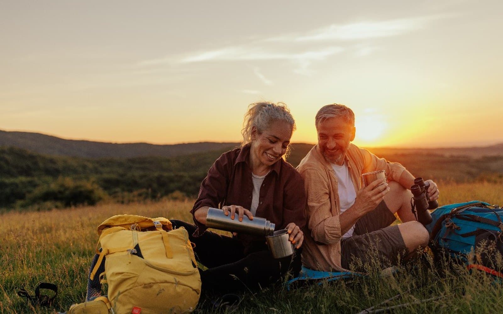 A couple resting on a hilltop at sunset, looking out over the trail ahead.